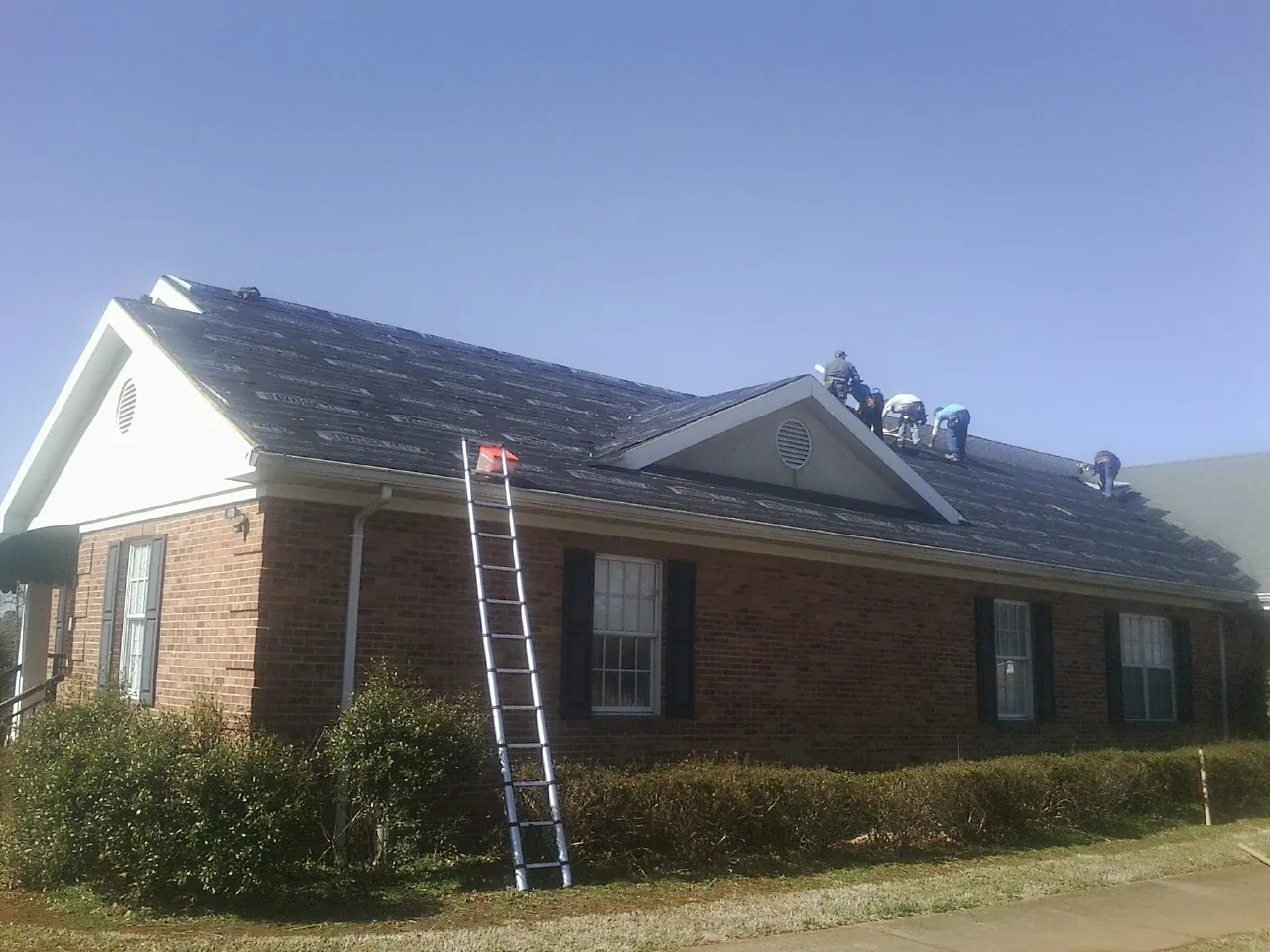 Crew tearing shingles off a brick ranch roof with a ladder set — Metal Roof Repair work by our crew in Barnegat Light