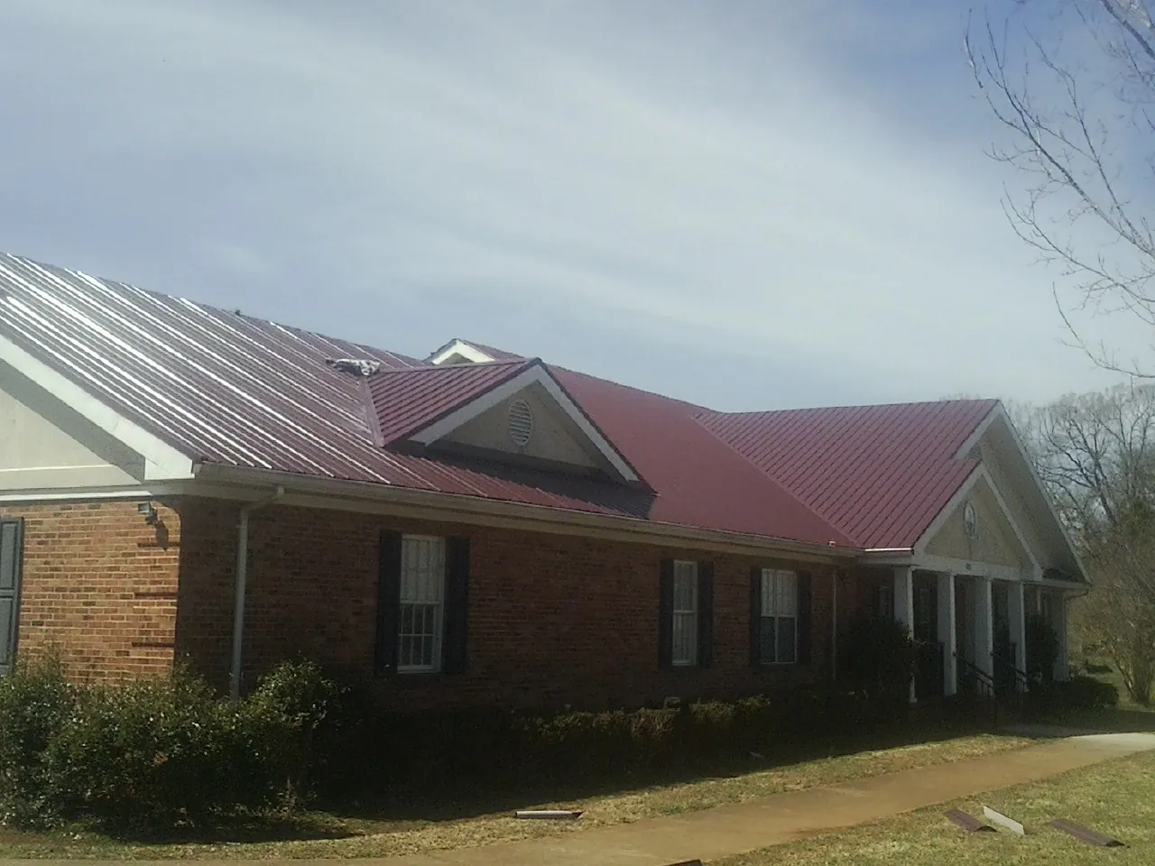 Red metal roof with gabled entries on a long brick building, from a Hail Damage Roof Repair job in Barnegat Light