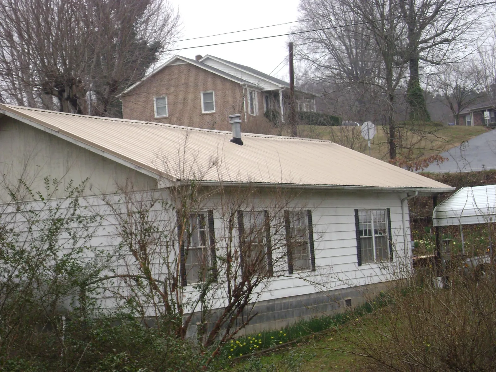 Tan metal roof on a white sided house set into a hillside — Commercial Roofing by Roofing Brothers in Barnegat Light